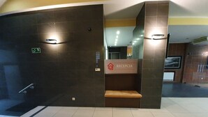 Una zona de recepción con una pared de baldosas oscuras, un banco y un cartel que dice 'RECEPCJA'.