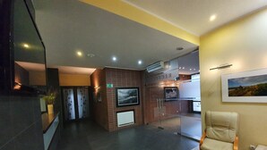 Un área de recepción con mostrador, zona de estar con una silla, televisión montada en una pared de ladrillo y un cuadro enmarcado en la pared.