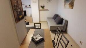 Un espacio habitable compacto con una mesa de comedor, sillas, un sofá y una pequeña cocina al fondo.
