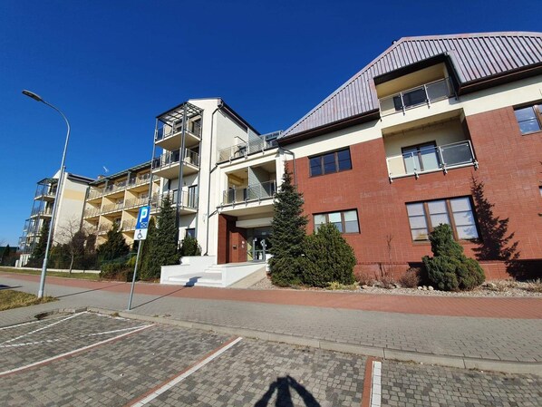 A multi-story residential building with balconies, a parking area, and a clear blue sky. - LIDO Apartamenty (Sarbinowo)