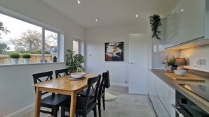A modern kitchen with a dining area, featuring a wooden table, black chairs, a large window, and a potted plant. - Beech Dreams - Stylish Place to Stay (Conwy)