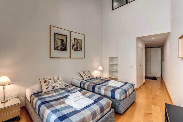 A modern hotel room with two beds, a desk, and a small seating area. There are framed pictures on the wall and a door leading to a hallway. - Great experience for family or friends Trastevere (Roma)