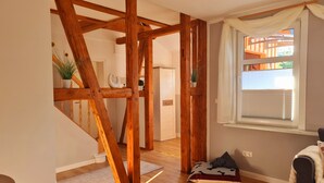 A room with exposed wooden beams, a window with blinds, a potted plant, and a bed with a blanket.