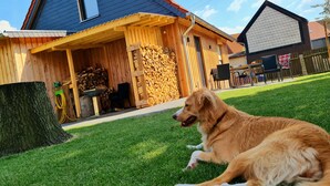 A dog lying on grass in front of a wooden house with a sloped roof.