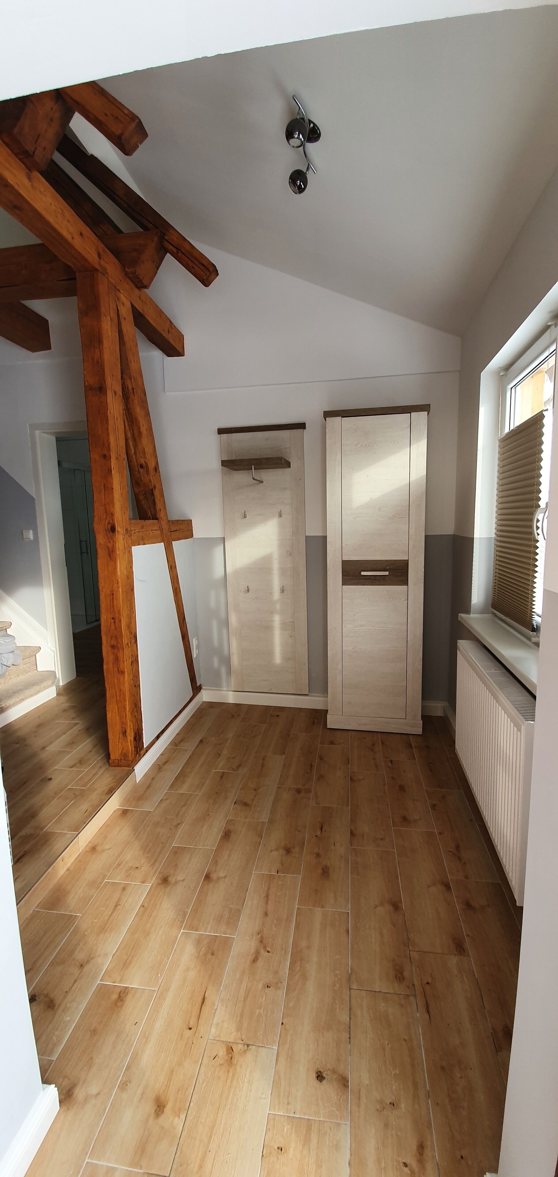 Una habitación con piso de madera, techo estilo loft, un armario y una ventana con persianas.