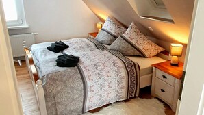 A bedroom with a sloped ceiling, a skylight, a bed with patterned bedding, a white furry rug, and bedside lamps.