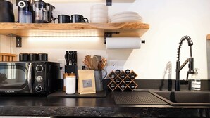A kitchen with a Galanz microwave, a coffee maker, a kettle, and a coffee grinder. There are wooden shelves above the counter holding plates and cups. A sink with a modern faucet is visible. - Clark Farm Silos #2 - Incredible  Mountain Views (Kalispell)