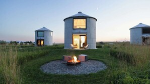 A yurt-style building with a fire pit in the center, surrounded by grass and gravel. - Clark Farm Silos #2 - Incredible  Mountain Views (Kalispell)