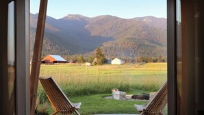A view from a room with two wooden chairs facing a grassy field with mountains in the background. - Clark Farm Silos #2 - Incredible  Mountain Views (Kalispell)