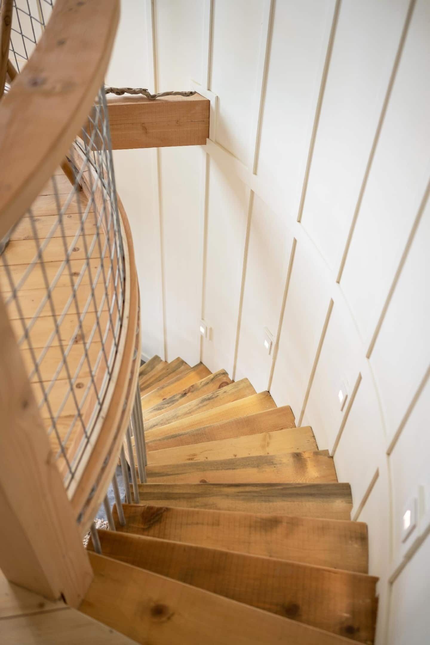 A wooden spiral staircase with metal railings, leading to a landing.