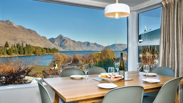 A dining table set with plates, glasses, and a bottle, overlooking a lake with mountains in the background. - Villas Lake Terrace with Fantastic View (Queenstown)