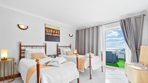 Een hotelkamer met twee bedden, een groot raam met gordijnen, uitzicht op zee en een balkon met tuinmeubilair.
