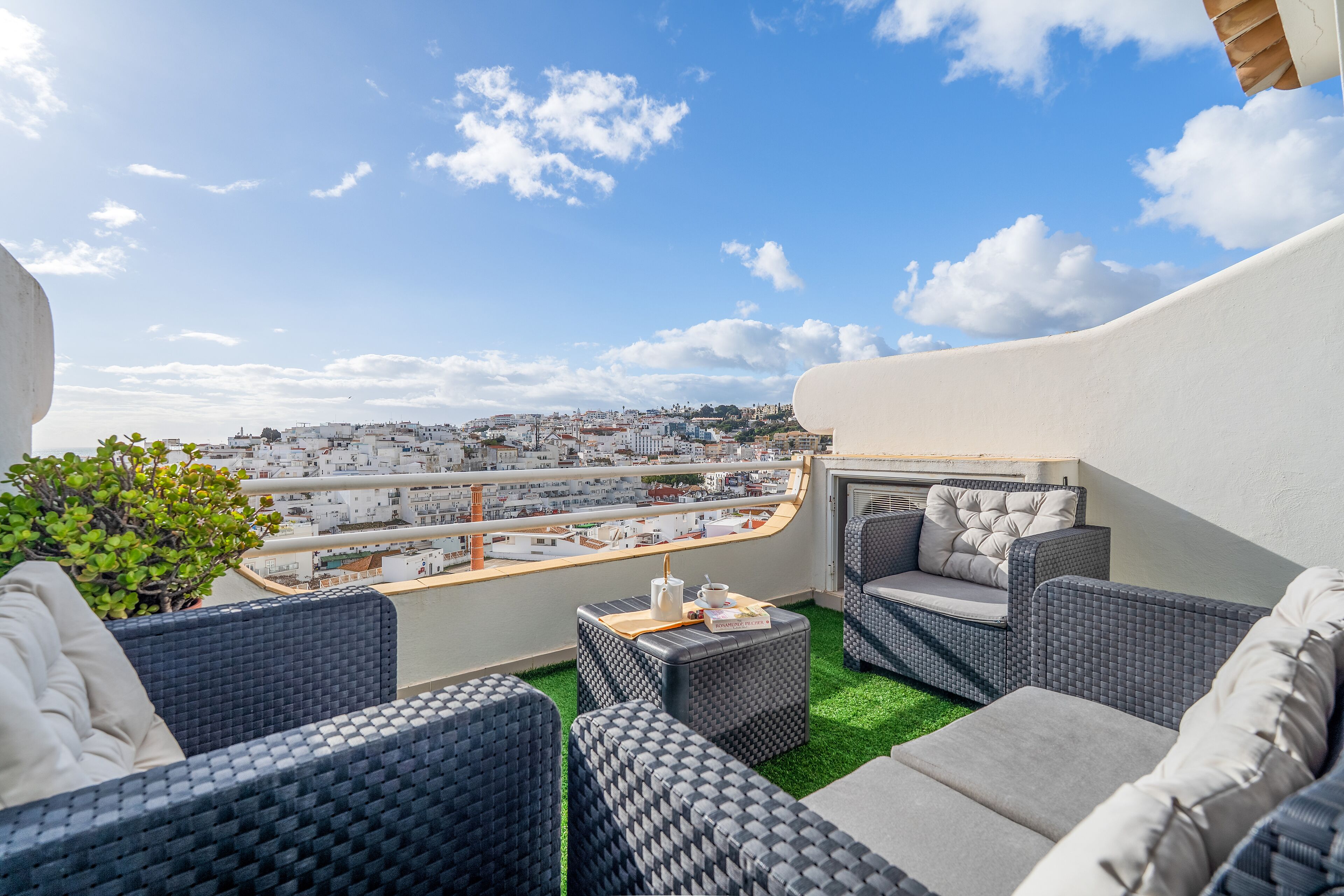 Eine Dachterrasse mit Korbmöbeln, einem kleinen Tisch und Blick auf die Stadtlandschaft.
