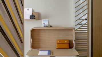 A modern, minimalist room with a geometric-patterned wall, a wooden desk with a laptop, a notebook, and a pen, and a white chair.