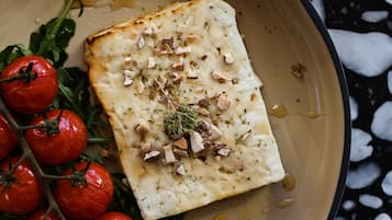 Une assiette contenant un morceau de poisson, des tomates cerises et des herbes aromatiques.