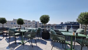 Una terraza al aire libre con mobiliario verde y árboles en macetas, con vistas a la ciudad.