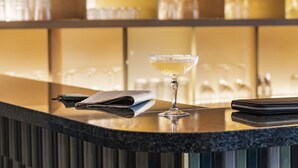 Zona de bar con un vaso de una bebida amarillenta, un menú doblado y una billetera negra sobre una encimera oscura.