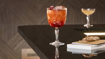 Two cocktails on a reflective bar counter with a herringbone-patterned wall and a woven chair in the background.
