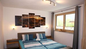 Une chambre à coucher comprenant un lit, une table de chevet, une fenêtre avec des rideaux et des œuvres d’art accrochées au mur.