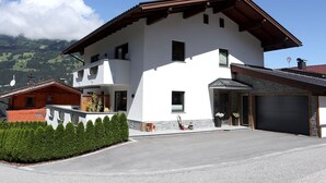 Une maison à deux étages avec un garage, un balcon et une vue sur les montagnes en toile de fond.