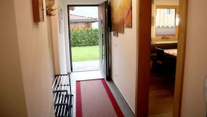 Un couloir recouvert d’une moquette rouge mène à une porte ouverte, et on peut apercevoir, à travers cette porte, un piano et un coin repas.