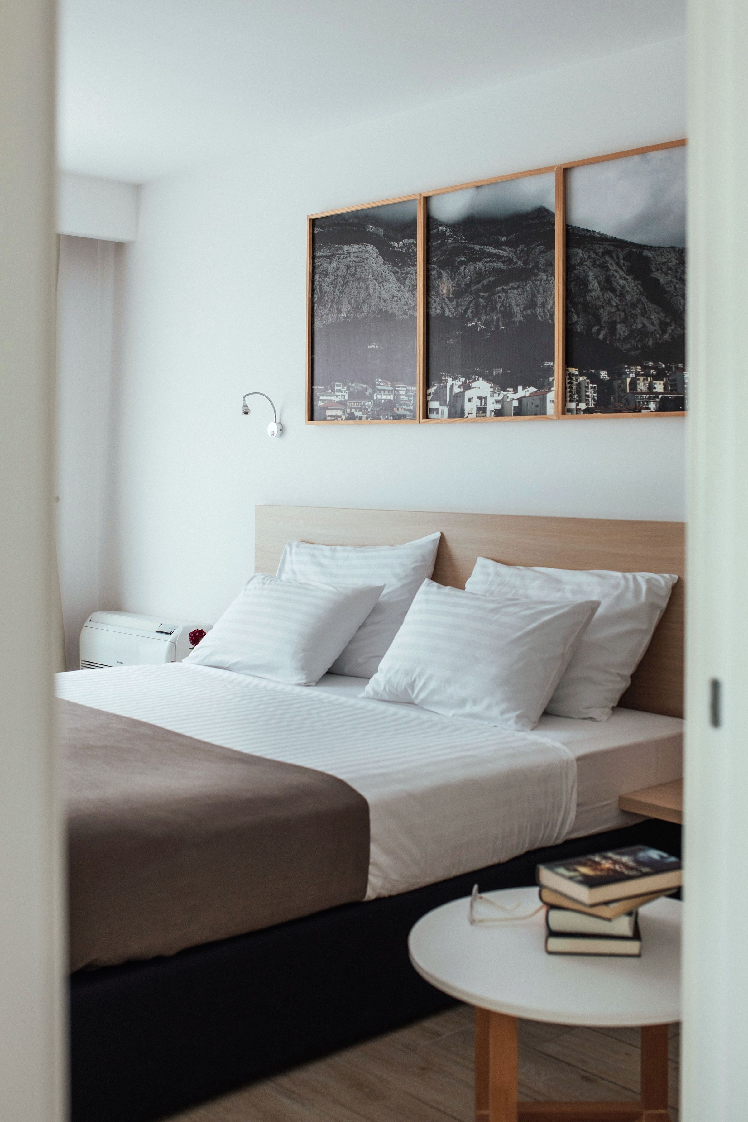 Een hotelkamer met een bed, een nachtkastje met boeken en een aan de muur hangend beeld van een bergachtig landschap.
