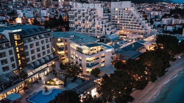 A hotel complex with multiple buildings, a swimming pool, and a beach view.