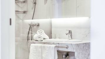 A modern bathroom with a glass-enclosed shower, a marble sink, and neatly folded towels on a shelf.