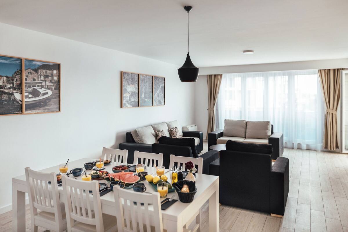A modern living room with a dining area, featuring a sofa set, a dining table with chairs, and artwork on the walls.