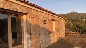 Un bâtiment en pierre avec des portes et des fenêtres en bois, une terrasse en bois et une vue sur un paysage vallonné.