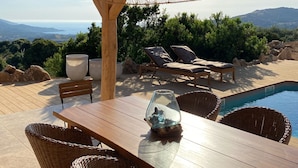 Une terrasse en bois avec une piscine, des chaises longues et des meubles en osier.