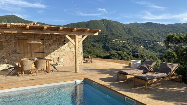Un espace aménagé au bord de la piscine, avec un mur en pierre, une pergola en bois et des chaises longues.
