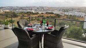 Une table à manger dressée avec des assiettes, des verres et des couverts, donnant sur un paysage urbain avec des bâtiments et de la verdure.