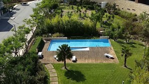 Un espace piscine doté d’une terrasse en bois, entouré d’une pelouse bien entretenue et d’arbres.