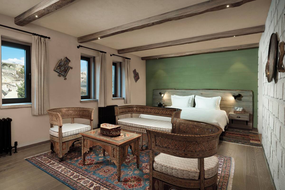A room with a bed, two chairs, a table, and a view of the outdoors.