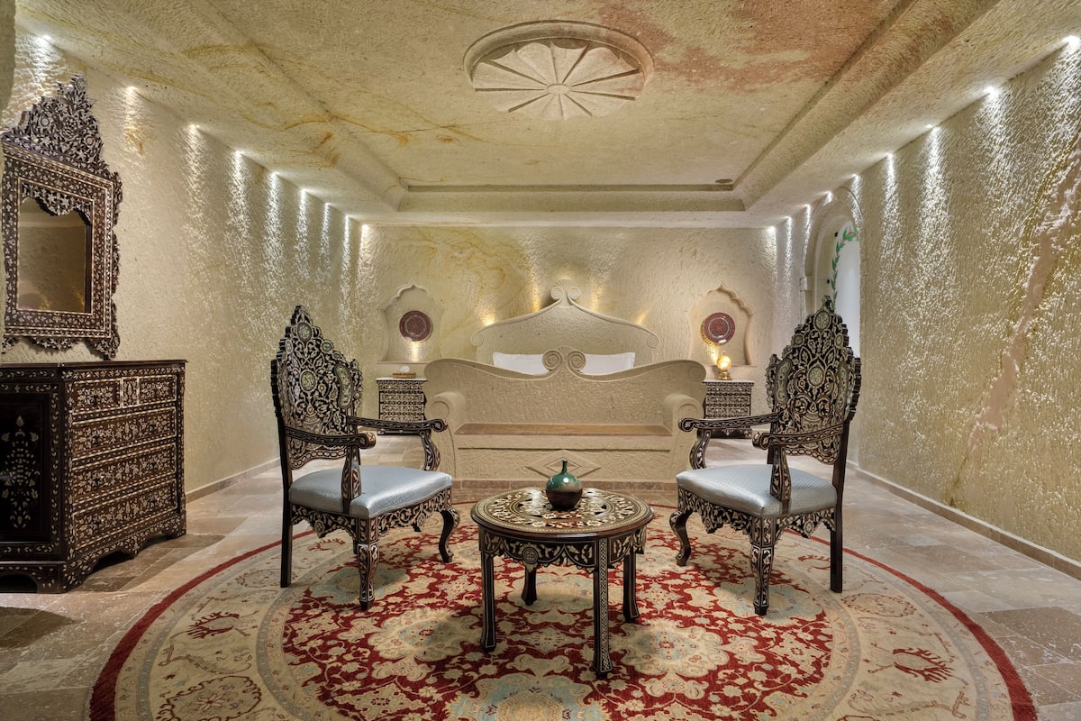 A luxurious room with a large bed, ornate chairs, a small table, and a decorative mirror.