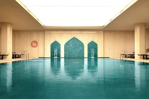 En indendørs swimmingpool med krystalklart vand, et ovenlys og en flisebeklædt væg med tre buede vinduer.