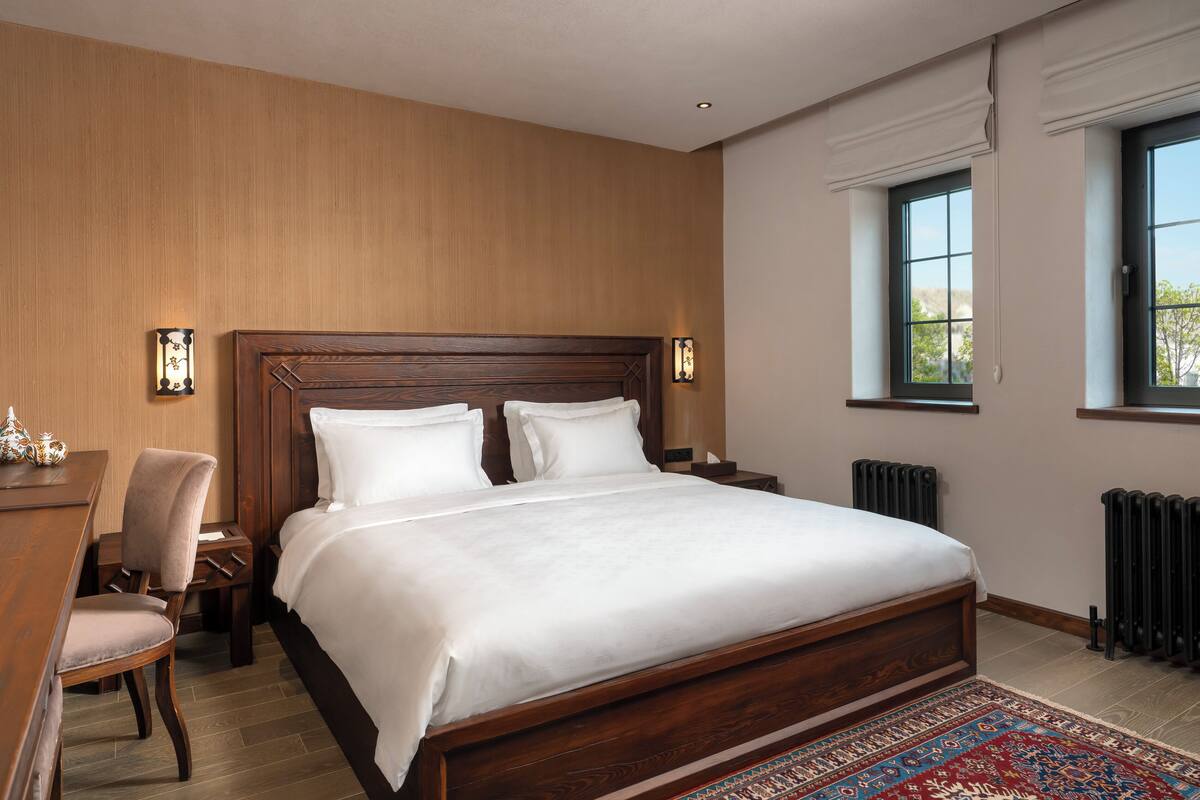 A bedroom with a wooden bed, two bedside tables, a chair, a desk, a window, and a radiator.
