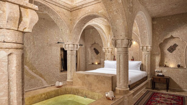 A luxurious stone-walled room with a large bed, a bathtub, and a red patterned rug. - AJWA Cappadocia - Preferred Hotels Legend Collection (Ürgüp)