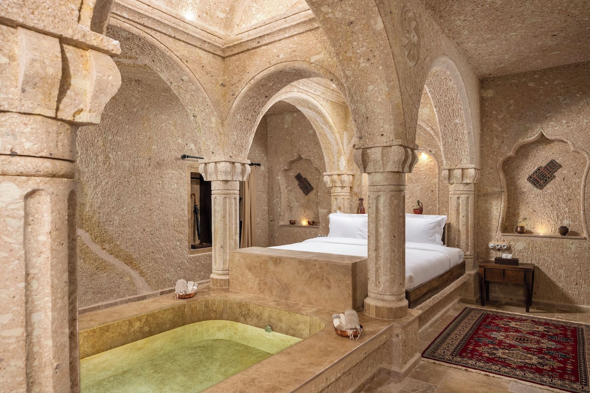 A luxurious stone-walled room with a large bed, a bathtub, and a red patterned rug.
