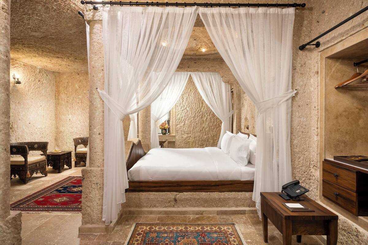 A bedroom with a four-poster bed, a wooden nightstand, and a red and blue patterned rug.
