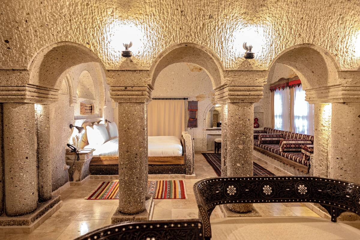 A room with a bed, a sofa, and a chair, with stone columns and arches.