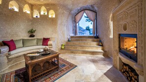A stone-walled room with a sofa, a wooden coffee table, a fireplace, and a view of the outdoors. - AJWA Cappadocia - Preferred Hotels Legend Collection (Ürgüp)