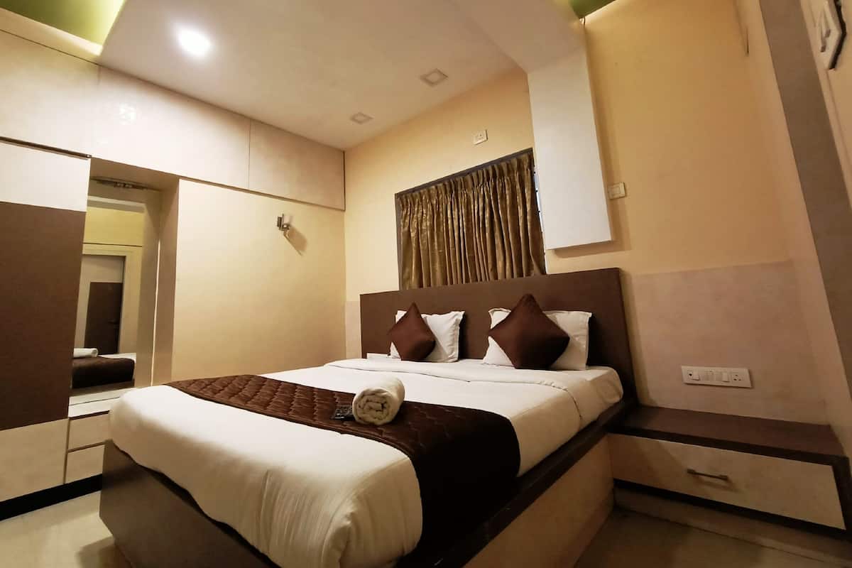 Habitación de hotel con cama, mesita de noche, espejo y lámpara de pared.