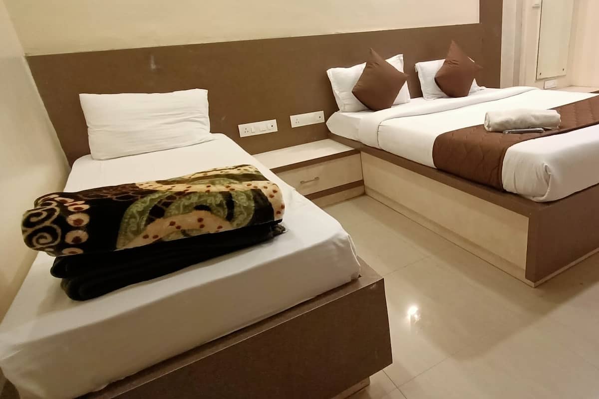 Una habitación de hotel con dos camas, una mesita de noche y un ventanal con cortinas.
