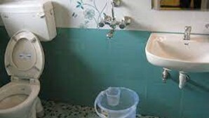 A bathroom with a toilet, sink, and a plastic container on the floor. - Anmols impex cottage (Ootacamund)