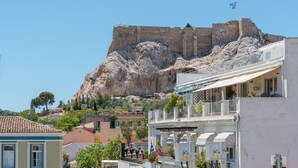 Une ville côtière dotée d’une imposante forteresse historique située sur une colline, de bâtiments modernes avec des balcons et d’un ciel d’un bleu éclatant.