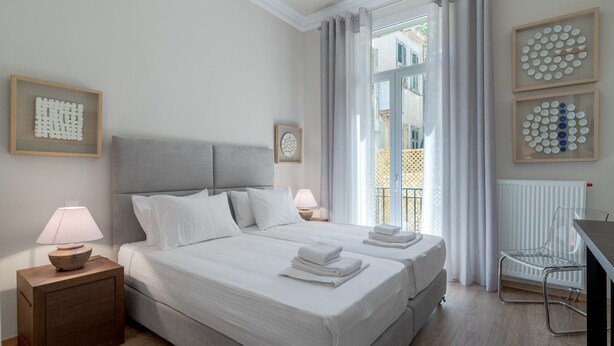 Habitación de hotel con dos camas, un escritorio, una silla y una ventana con cortinas.