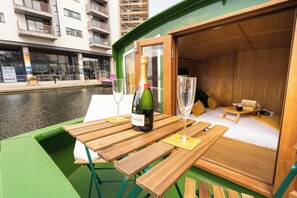 A green boat with a wooden deck, a bottle of wine, and two glasses on the table. - Luxury Boat, Floating Barge Accommodation (Edinburgh)