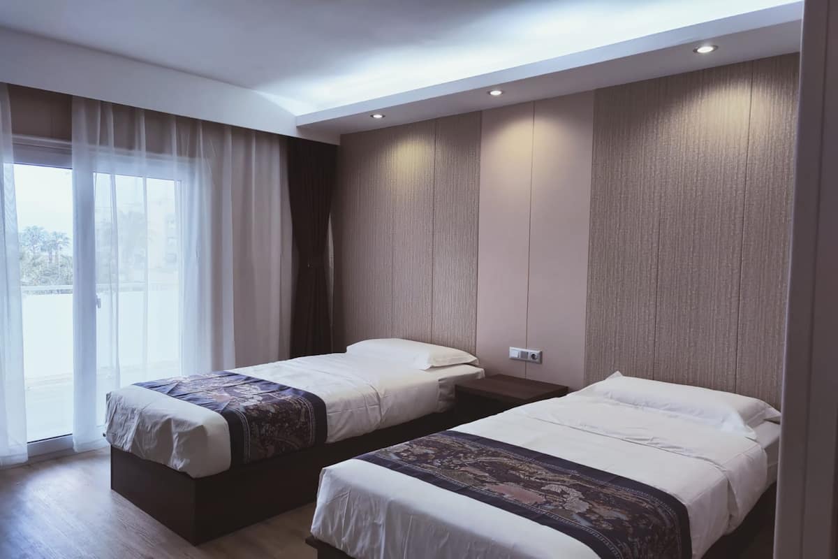 Une chambre d’hôtel avec deux lits, une grande fenêtre avec des rideaux légers et une vue sur l’extérieur.